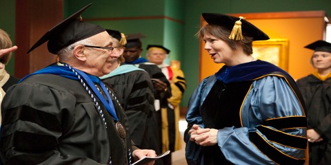 Two faculty members catch up while waiting for convocation to begin
